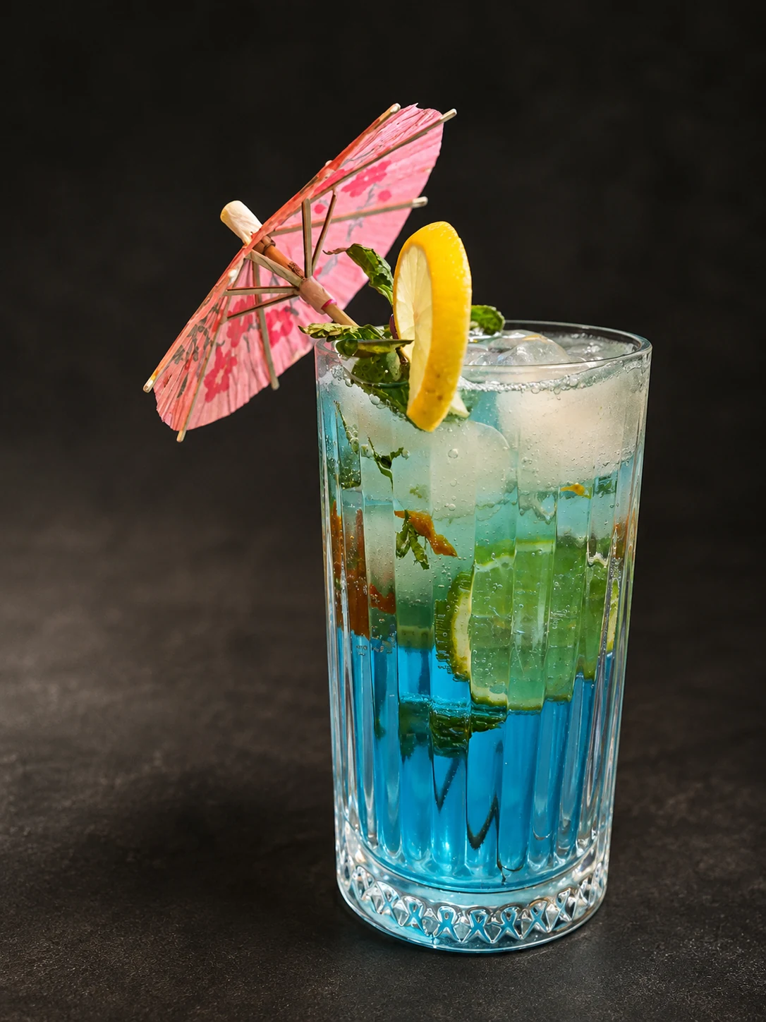 A blue mocktail garnished with lemon and mint
